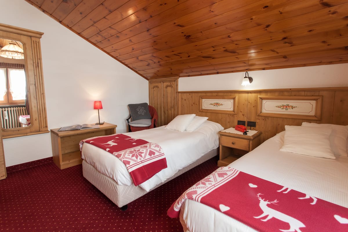 Une chambre avec deux lits, des têtes de lit en bois, une moquette rouge, une table de chevet avec une lampe et une chaise.