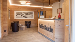Interior de madera con un mostrador de recepción identificado como "Vallee Blanche", cuadros enmarcados en la pared y techo de madera.