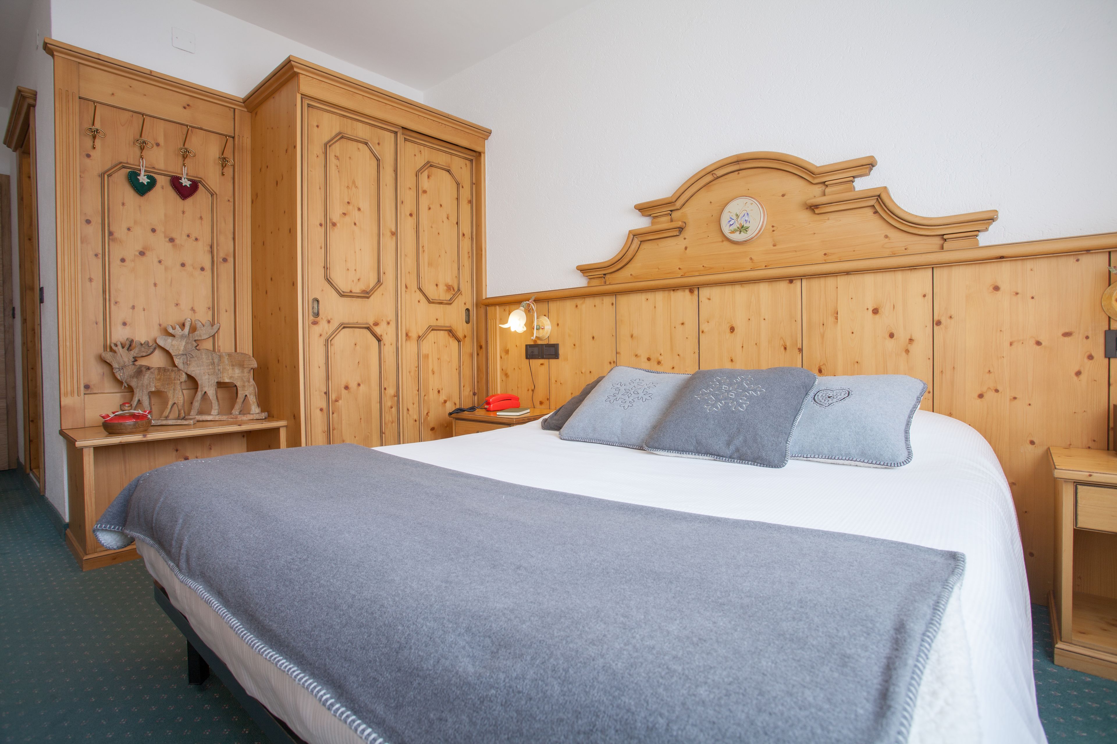 A bedroom with a wooden headboard, a bed with grey bedding, a nightstand with a lamp, and a wooden wardrobe with decorative items.