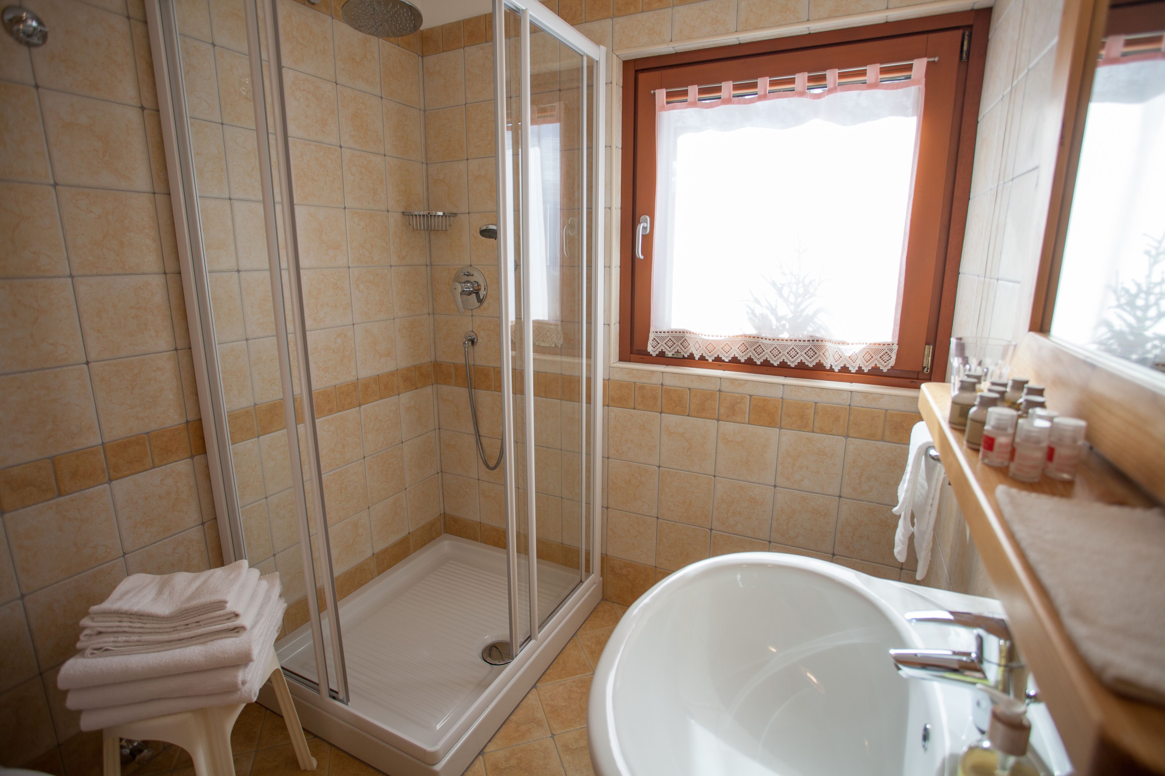 A bathroom with a glass-enclosed shower, a bathtub, and a window with a lace curtain.