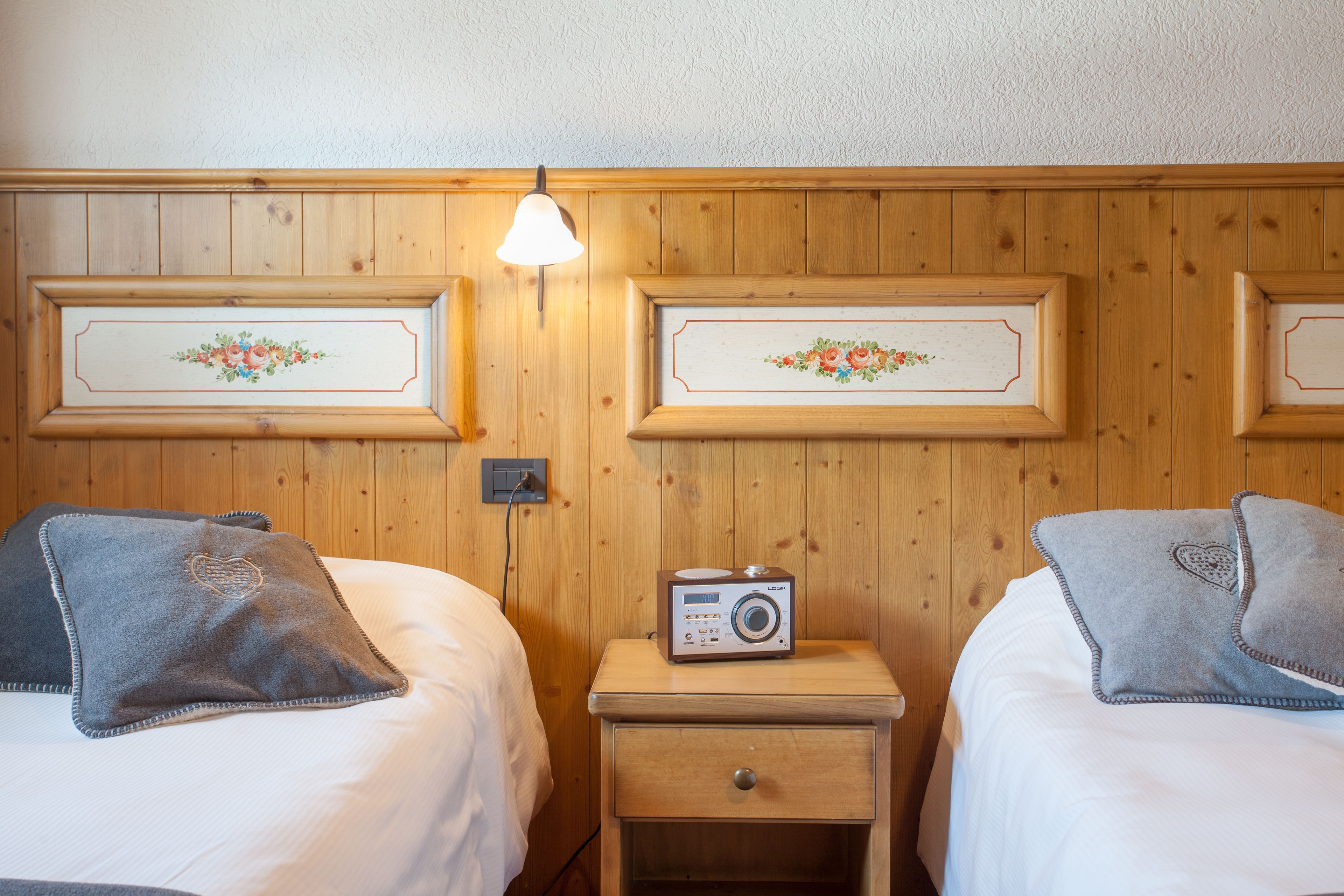 Camera d'albergo con due letti, un comodino con una radio e un punto luce fissato al muro.