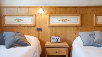 Camera d'albergo con due letti, un comodino con una radio e un punto luce fissato al muro.