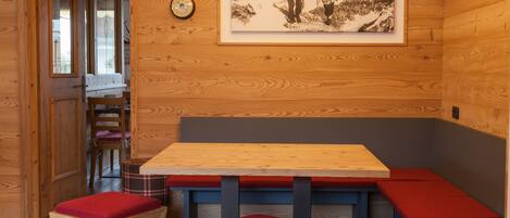 A wooden interior with a bench seating area, a table, and a framed photograph on the wall.