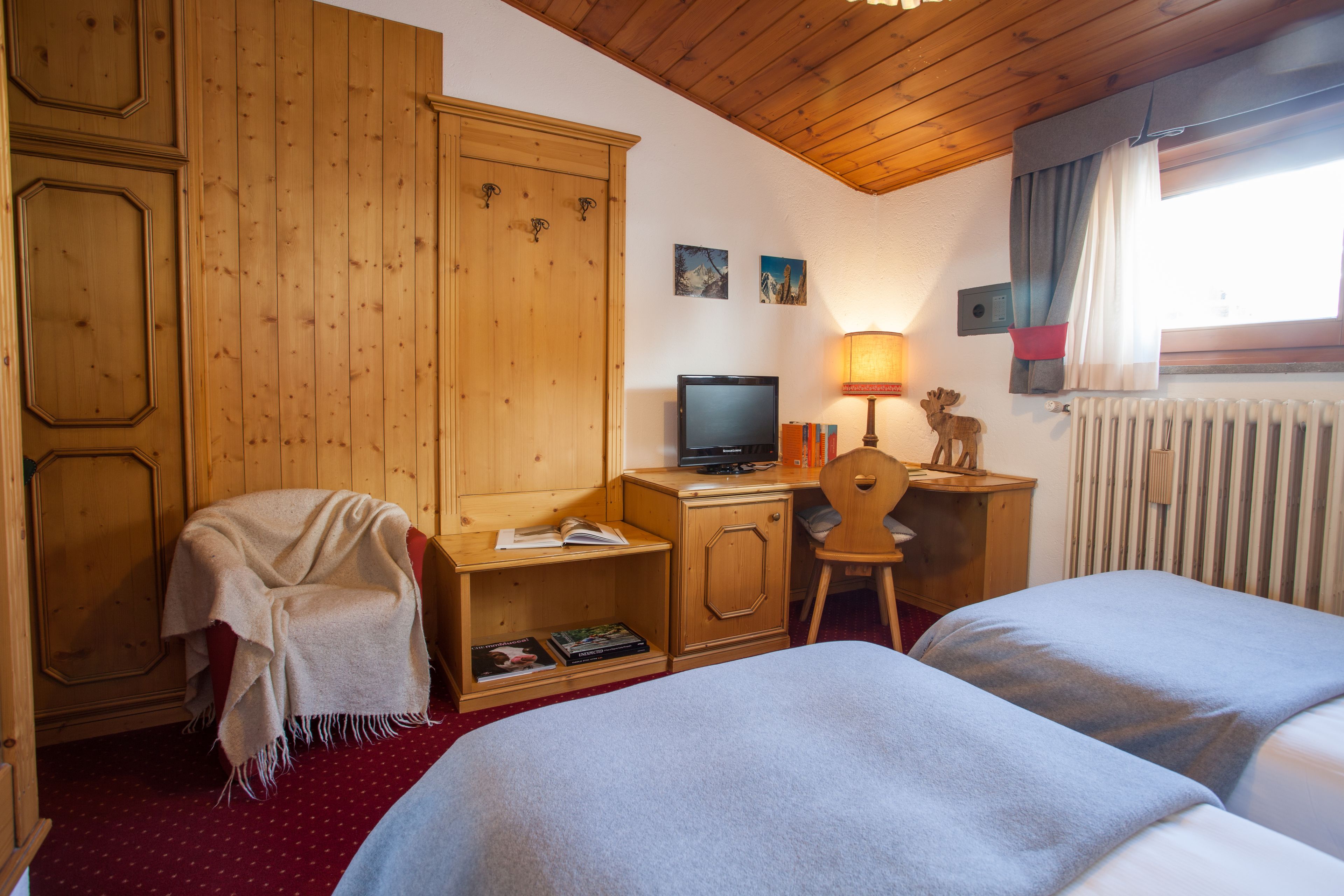 Una habitación con paredes y techo de madera, una cama, un escritorio con una computadora, una silla y un radiador.