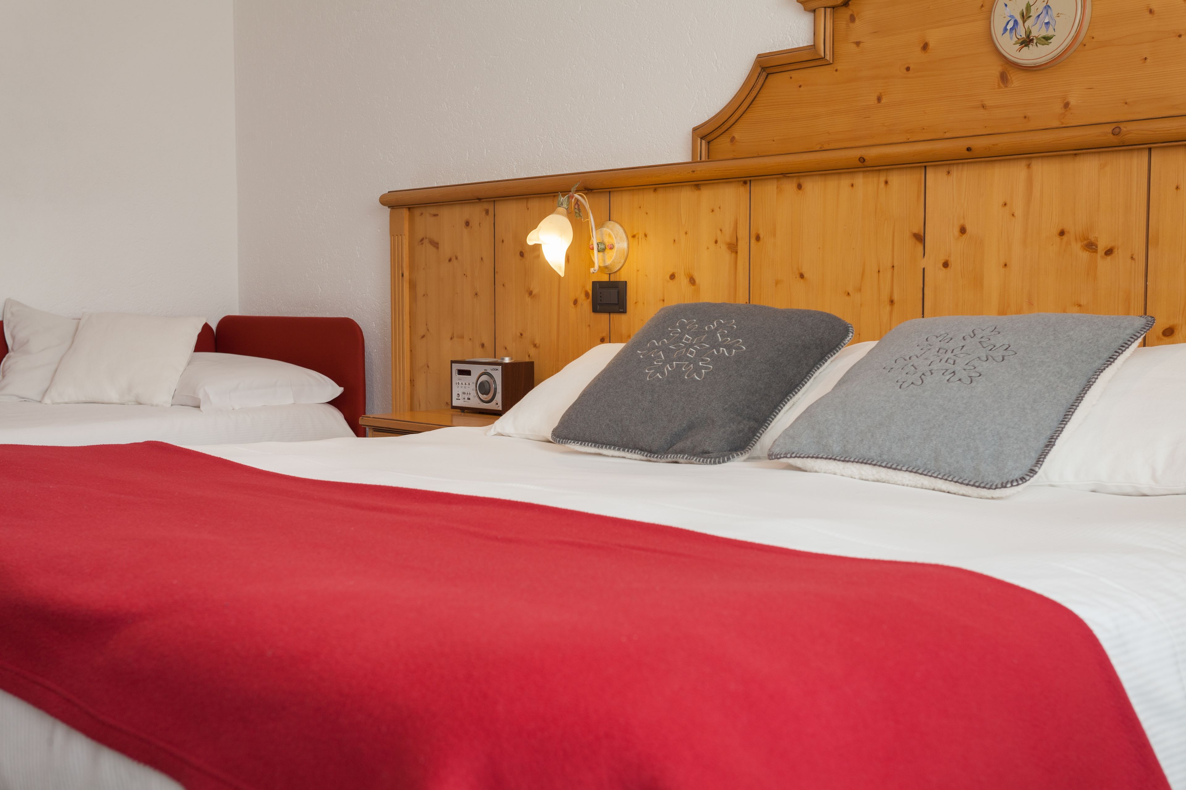 Habitación de hotel con cabecera de madera, una mesita de noche con una radio y una colcha roja.