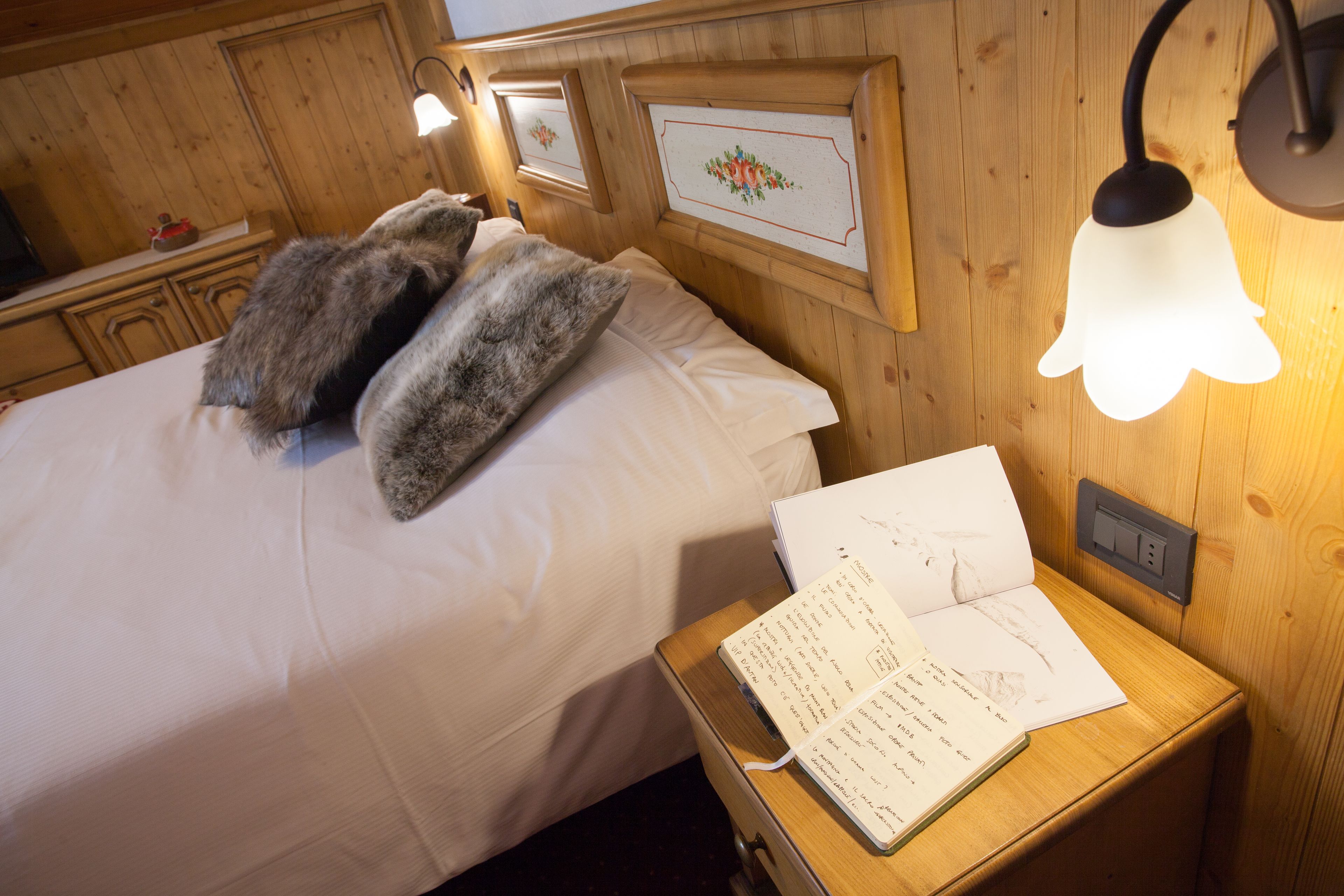 Une pièce en bois avec un lit, une table de chevet sur laquelle se trouve un livre et un luminaire fixé au mur.