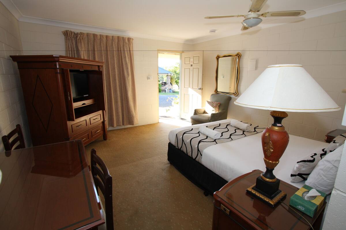 A hotel room with a bed, a desk, a television, a lamp, and a view of the outside.