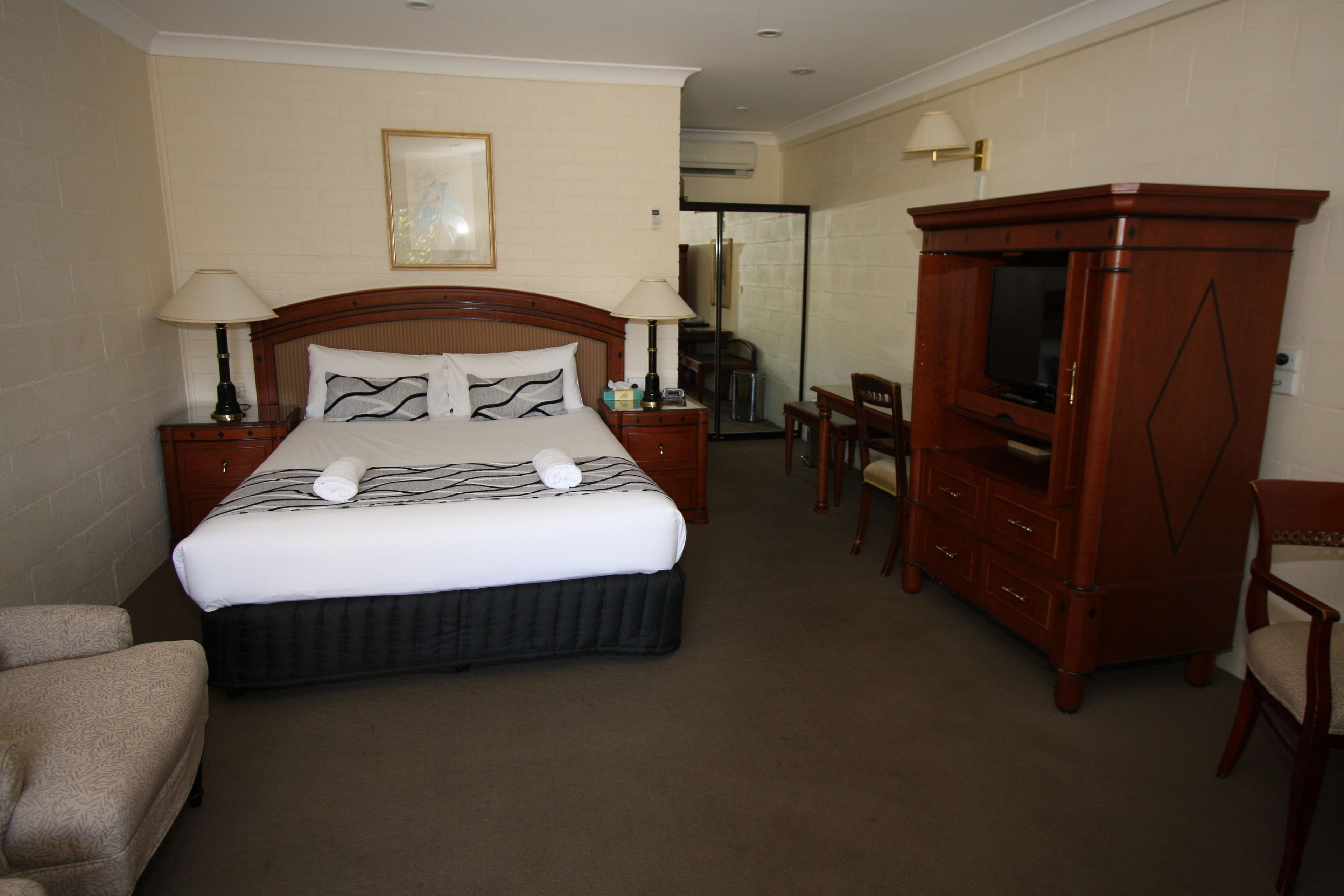 A hotel room with a large bed, two bedside tables with lamps, a wooden dresser, a television, and a chair.