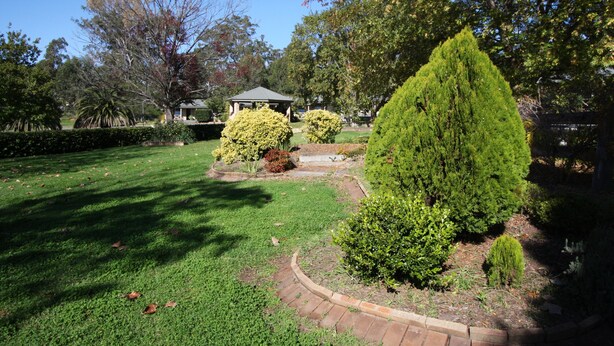 A well-maintained garden with a gazebo, neatly trimmed hedges, and a variety of trees. - Picton Valley Motel (Picton)