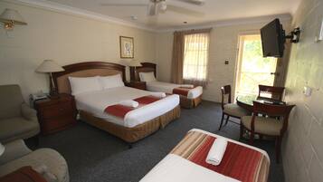 A hotel room with two beds, a desk, a chair, a TV, and a ceiling fan.