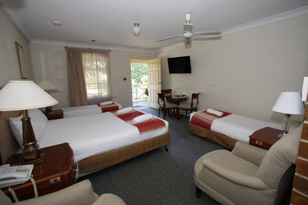 A hotel room with two single beds, a desk, a chair, a TV, and a ceiling fan.