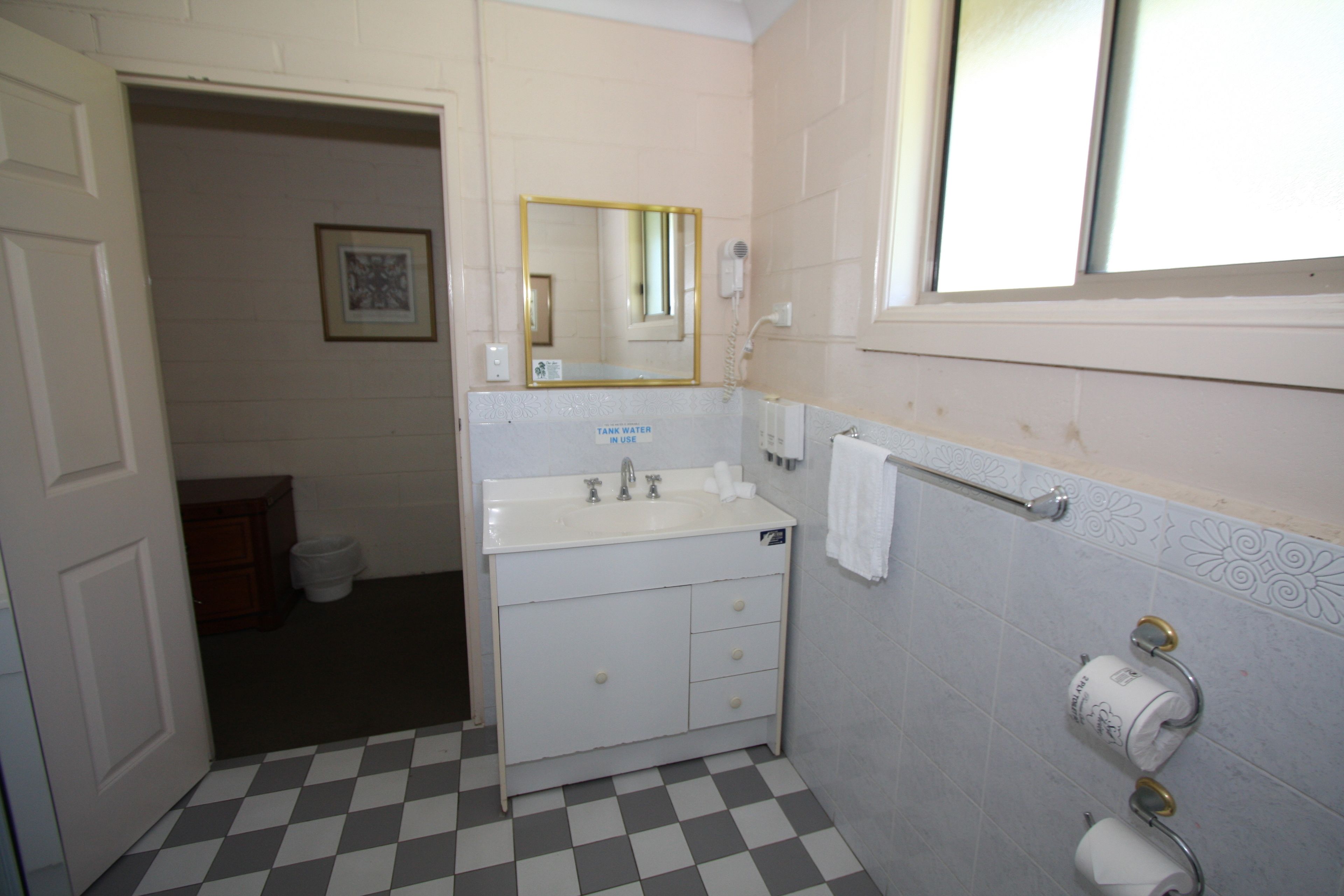 Un baño con piso a cuadros, un lavamanos con espejo y dos dispensadores de papel higiénico.