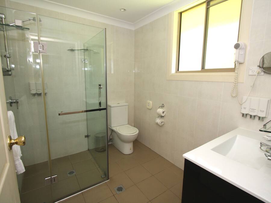 Een badkamer met een douchecabine van glas, een toilet, een wastafel en een raam.