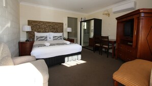 A hotel room with a large bed, a desk, a chair, a TV, and a wardrobe. - Picton Valley Motel (Picton)