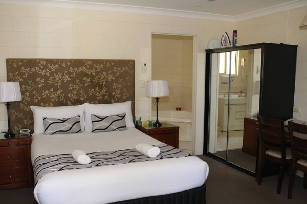 A hotel room with a large bed, two bedside tables, a desk, a chair, a bathroom with a glass door, and a wardrobe.