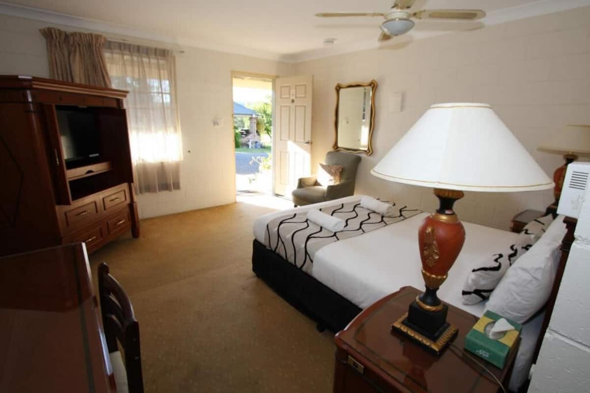 A hotel room with a bed, a desk, a lamp, a television, and a door leading to a balcony.