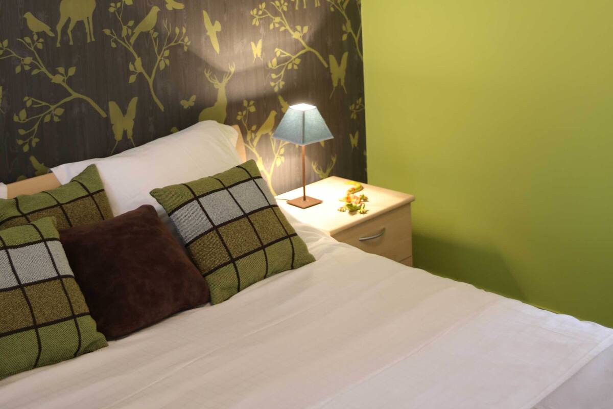 A neatly made bed with a white comforter and patterned pillows, a bedside lamp, and a nightstand with a small decorative item.