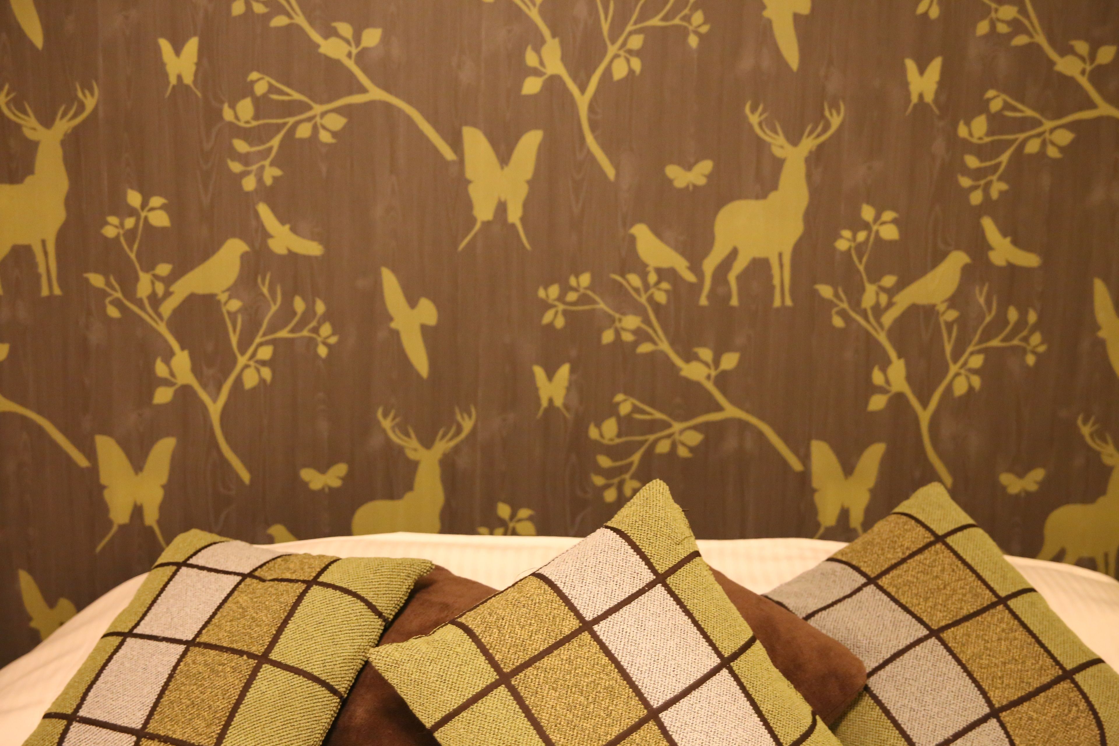 Una cama con dos almohadas y una pared con papel tapiz de temática natural.