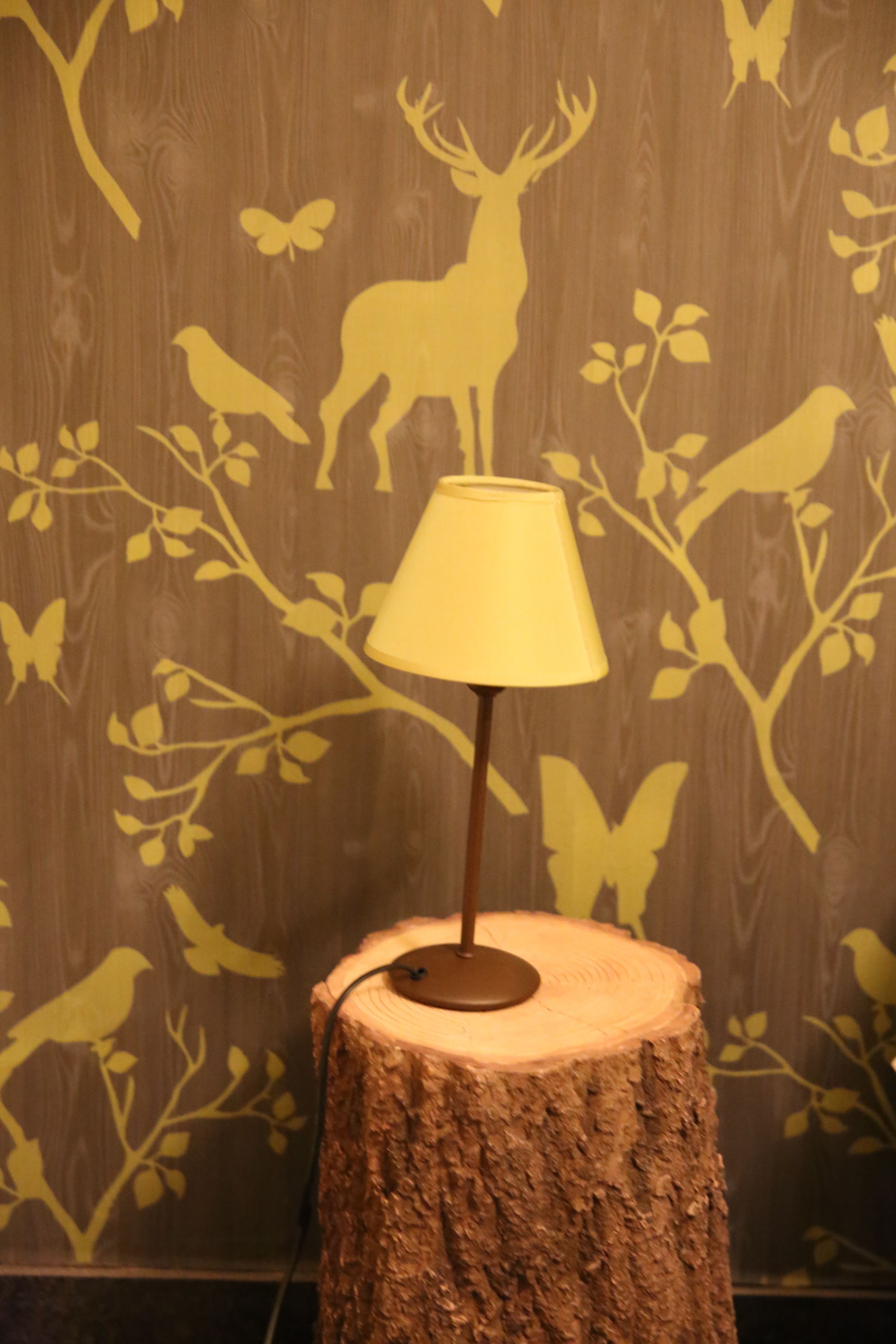 Une lampe posée sur un tronc d’arbre dans une pièce dont un mur est décoré de silhouettes d’animaux sauvages.