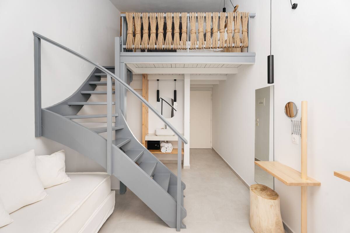 A modern interior with a grey spiral staircase, a white sofa, a wooden bench, and a small wooden stool.