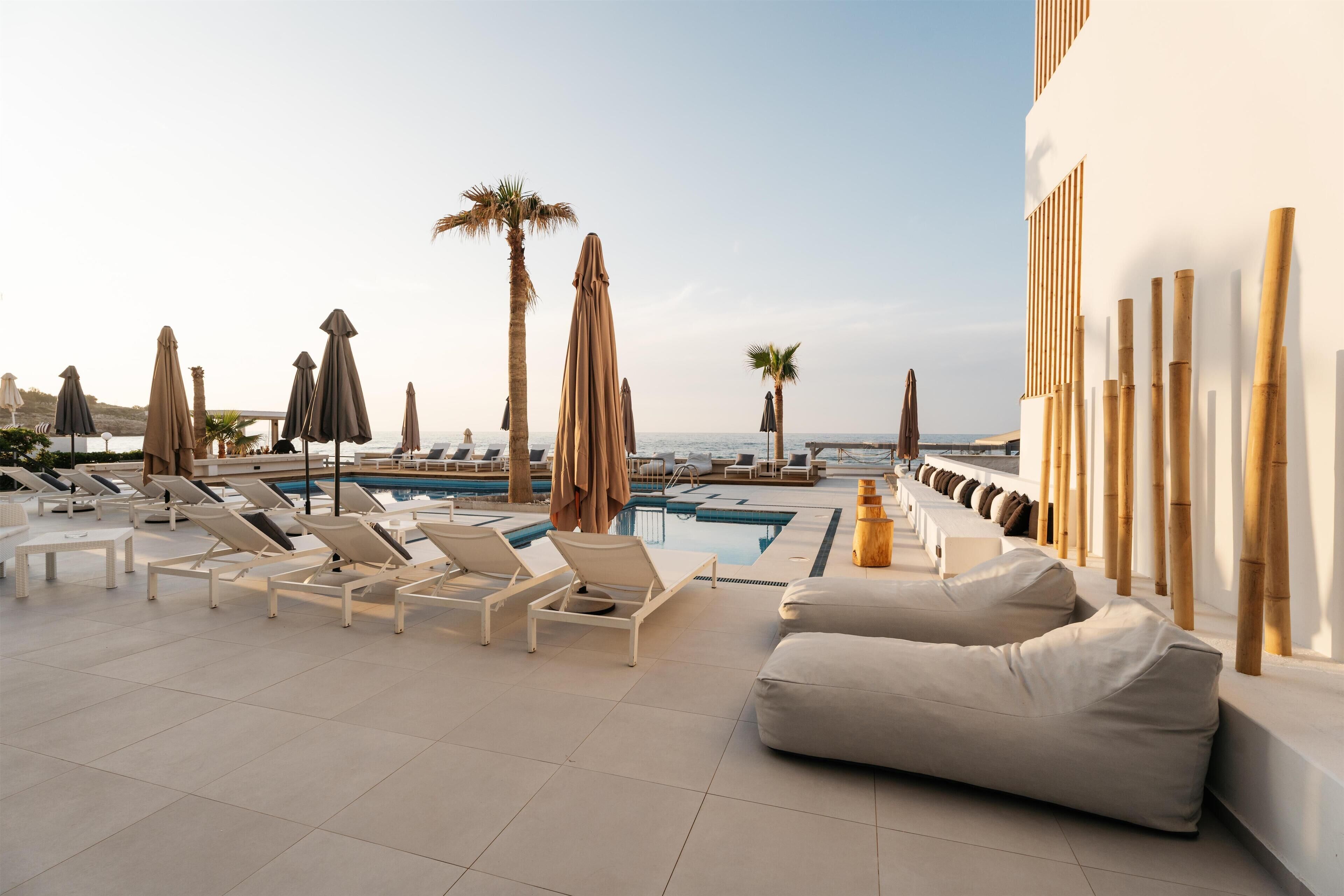 A rooftop pool area with lounge chairs, umbrellas, and a view of the sea.