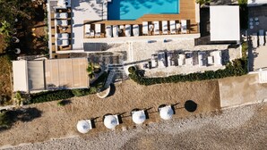 An aerial view of a beachfront hotel with a swimming pool, beach umbrellas, and lounge chairs. - Petradi Beach Lounge Hotel by GHH (Rethymno)