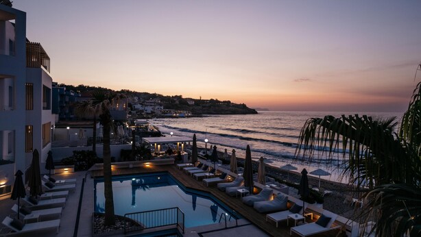 A poolside area with lounge chairs and umbrellas, overlooking a beach and ocean at sunset. - Petradi Beach Lounge Hotel by GHH (Rethymno)