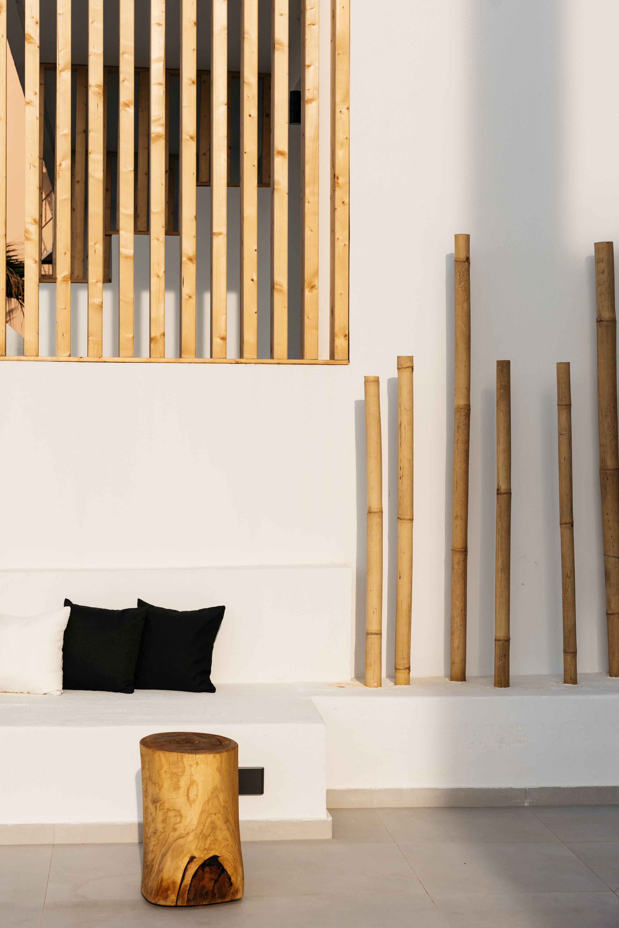 A modern interior with a white bench, black cushions, and bamboo elements.