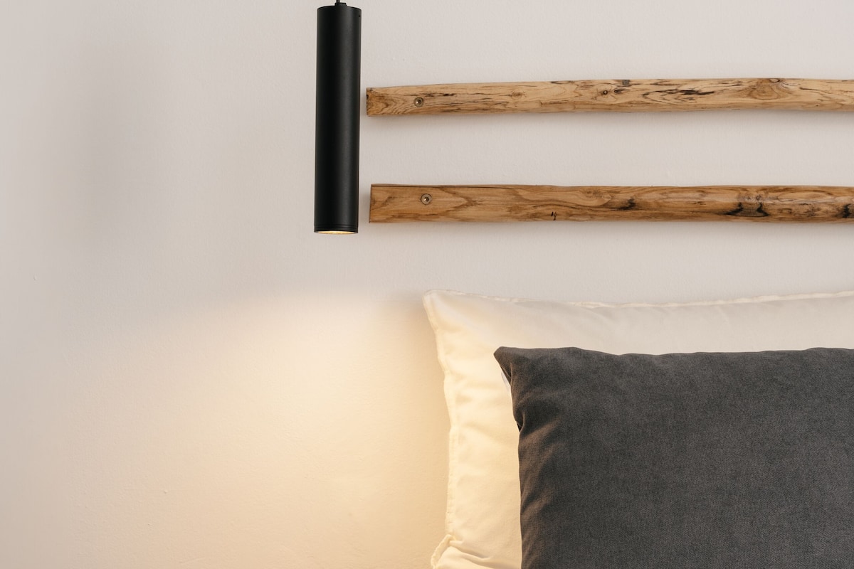 A bedroom with a bed, a wooden headboard, a bedside table, and a hanging light fixture.