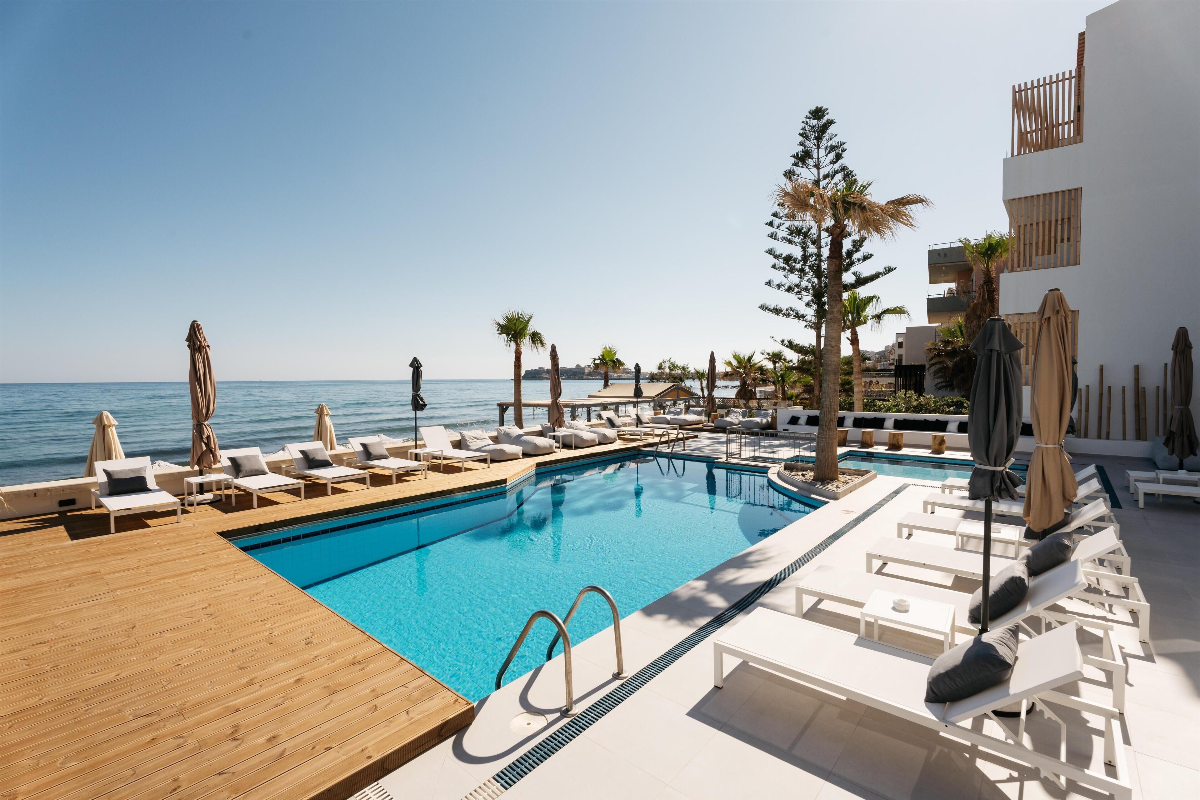 A poolside area with lounge chairs and umbrellas, a clear blue pool, and a view of the sea.