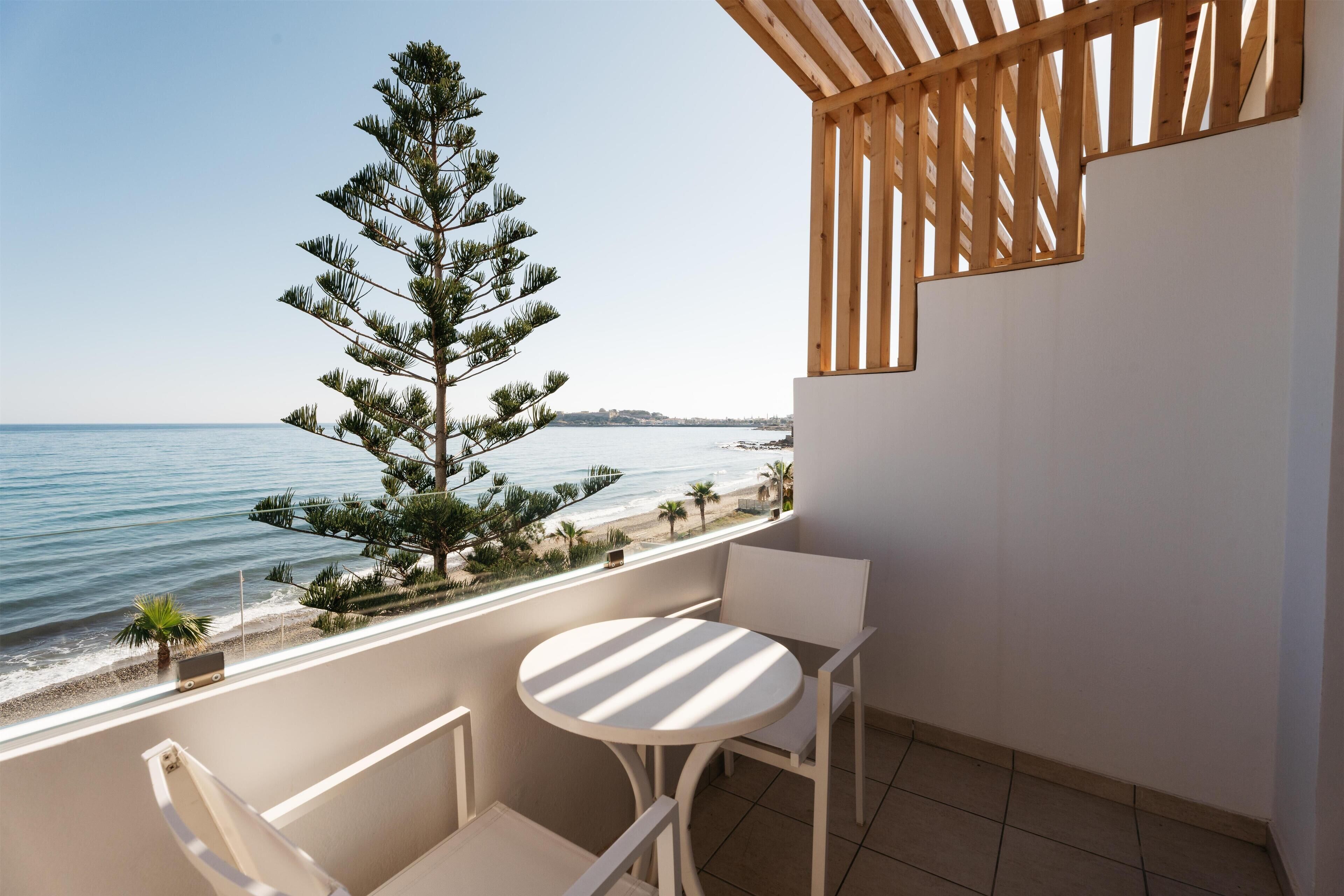 Een balkon met uitzicht op het strand, een ronde tafel en twee stoelen.