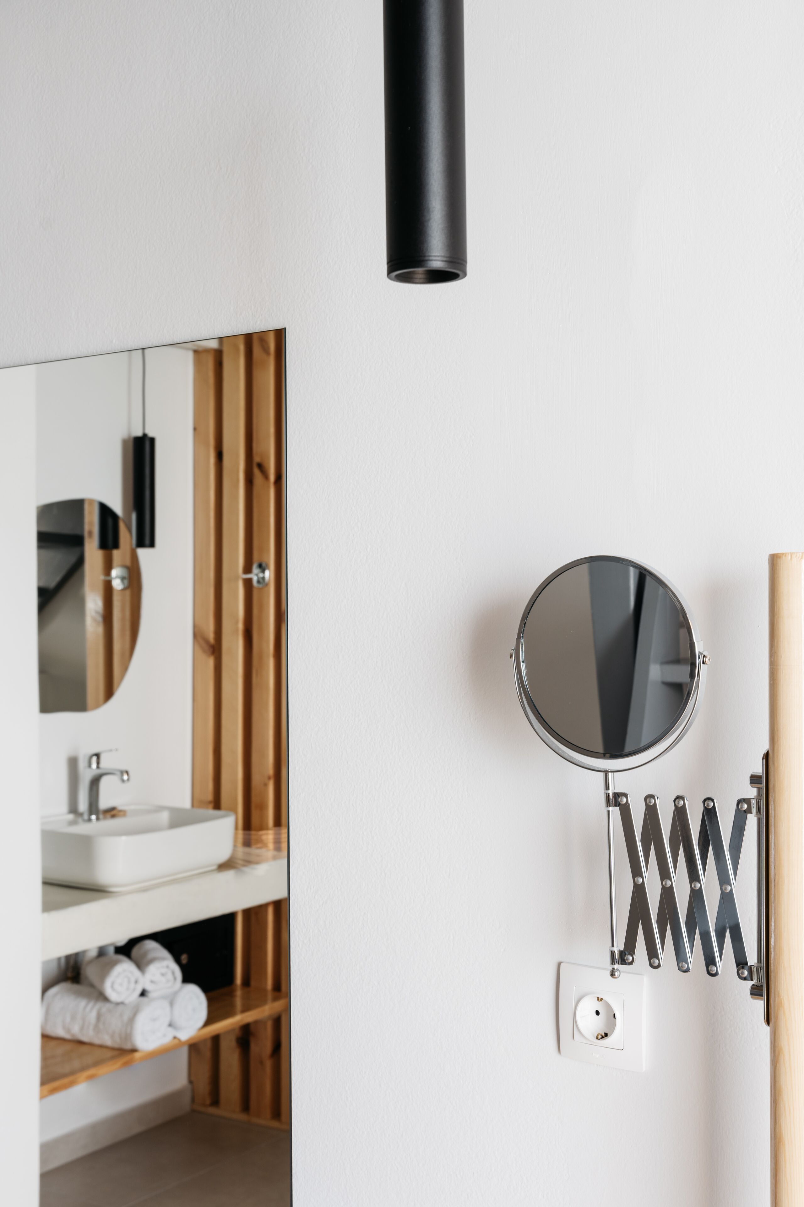 A modern bathroom with a wooden vanity, a round mirror, and a black wall-mounted light fixture.
