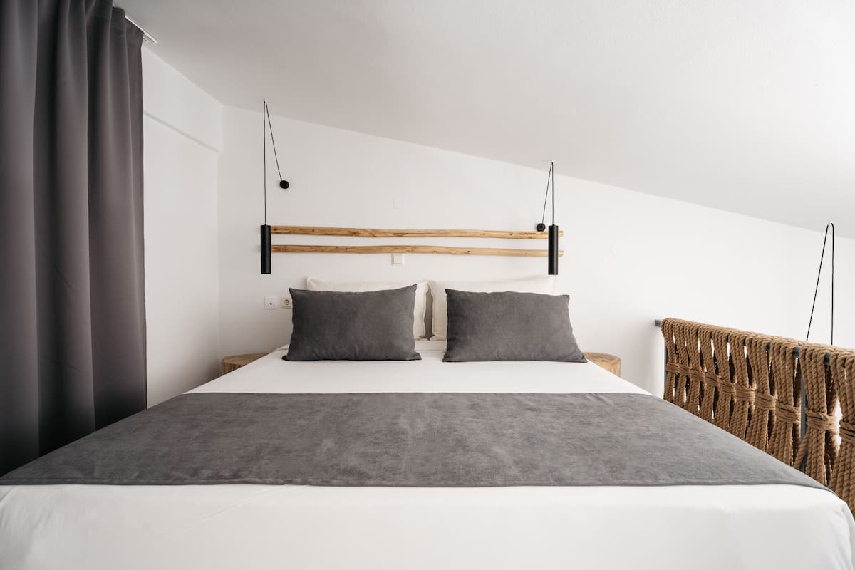 A modern bedroom with a wooden headboard, two pillows, a grey blanket, and a wicker chair.