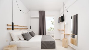 A modern bedroom with a bed, a TV, a mirror, and a window with curtains. - Petradi Beach Lounge Hotel by GHH (Rethymno)