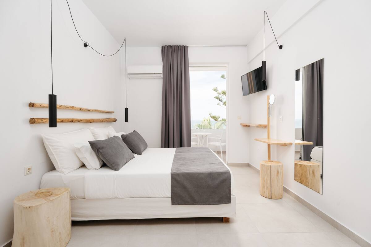 A modern bedroom with a bed, a TV, a mirror, and a window with curtains.