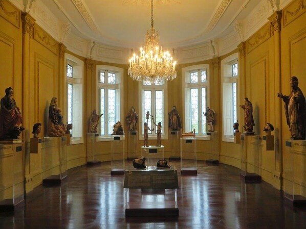 A grand hall with a large chandelier, statues on pedestals, and tall windows.