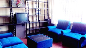 A living room with blue sofas, a coffee table, and a TV on a wooden stand. - Hostal Jovita (Santiago de Surco)