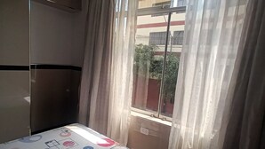 A hotel room with a bed, a wardrobe, a window with curtains, and a view of a building outside. - Hostal Jovita (Santiago de Surco)