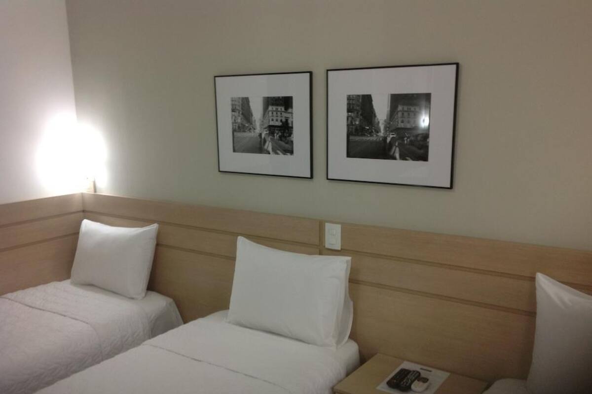 Hotellihuone, jossa on kaksi erillistä sänkyä, puinen pääty ja kaksi kehystettyä mustavalkokuvaa seinällä.