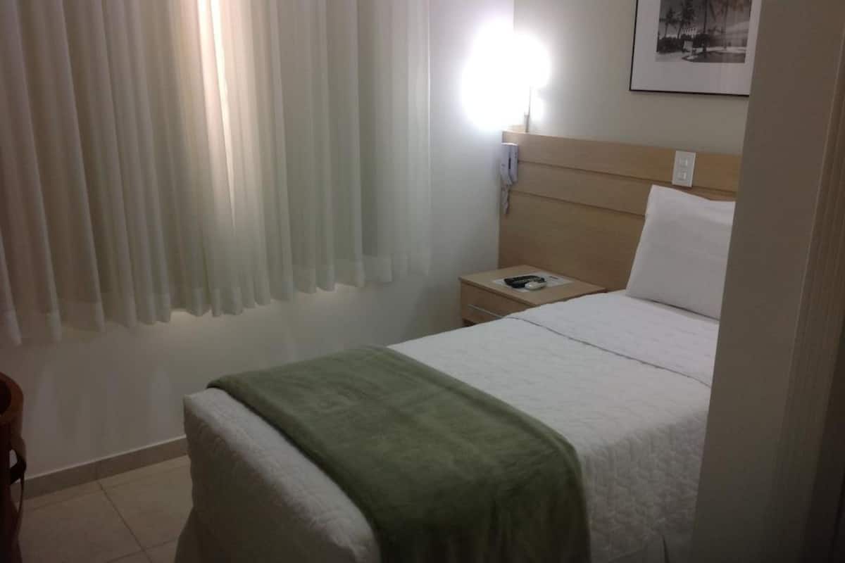 Hotellihuone, jossa on sänky, yöpöytä, lamppu ja taulu seinällä.