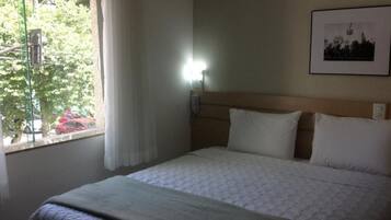 Habitación de hotel con una cama, una mesita de noche, un teléfono y una ventana con cortinas.