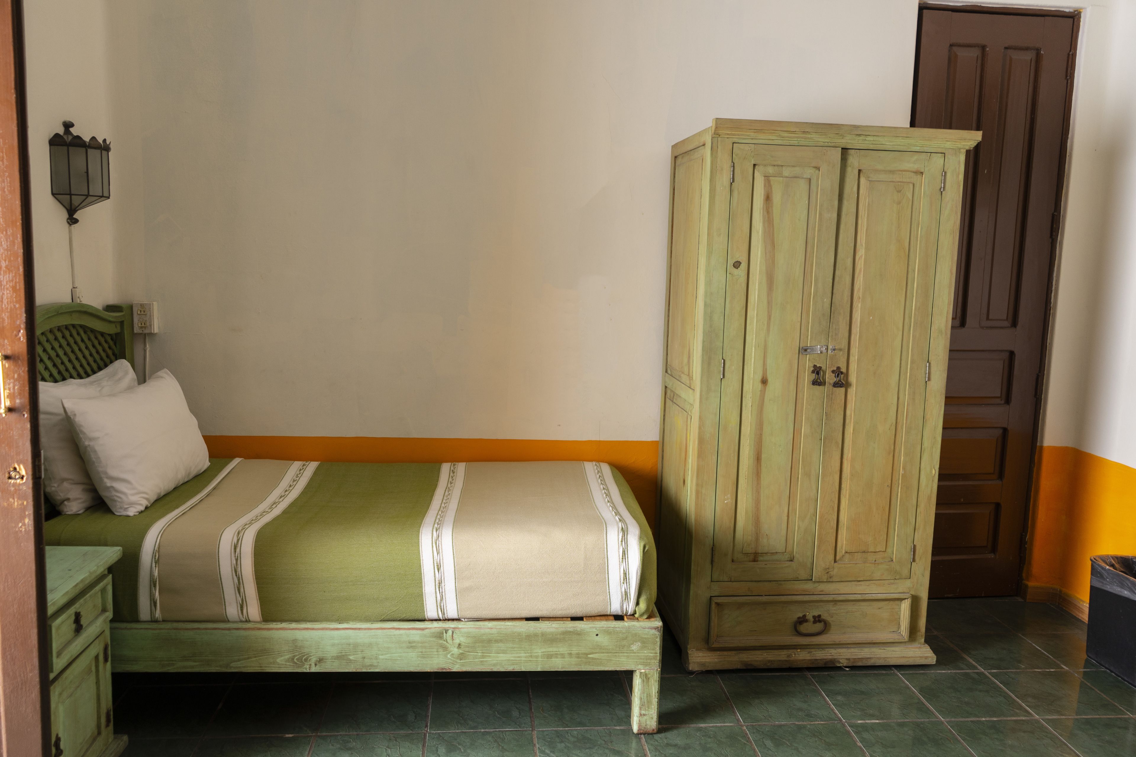 A room with a bed, a wardrobe, and a wall-mounted lamp.