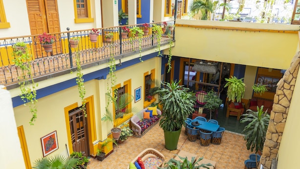 Un patio con zona de estar, plantas en macetas y un balcón con barandillas.