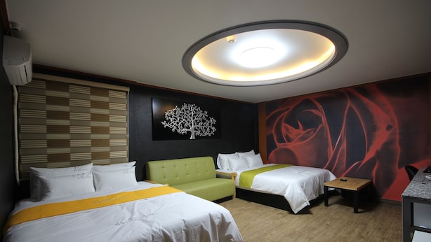 A hotel room with two beds, a green sofa, a small table, and a wall with a tree and abstract art. - BSB Hotel (Busan)