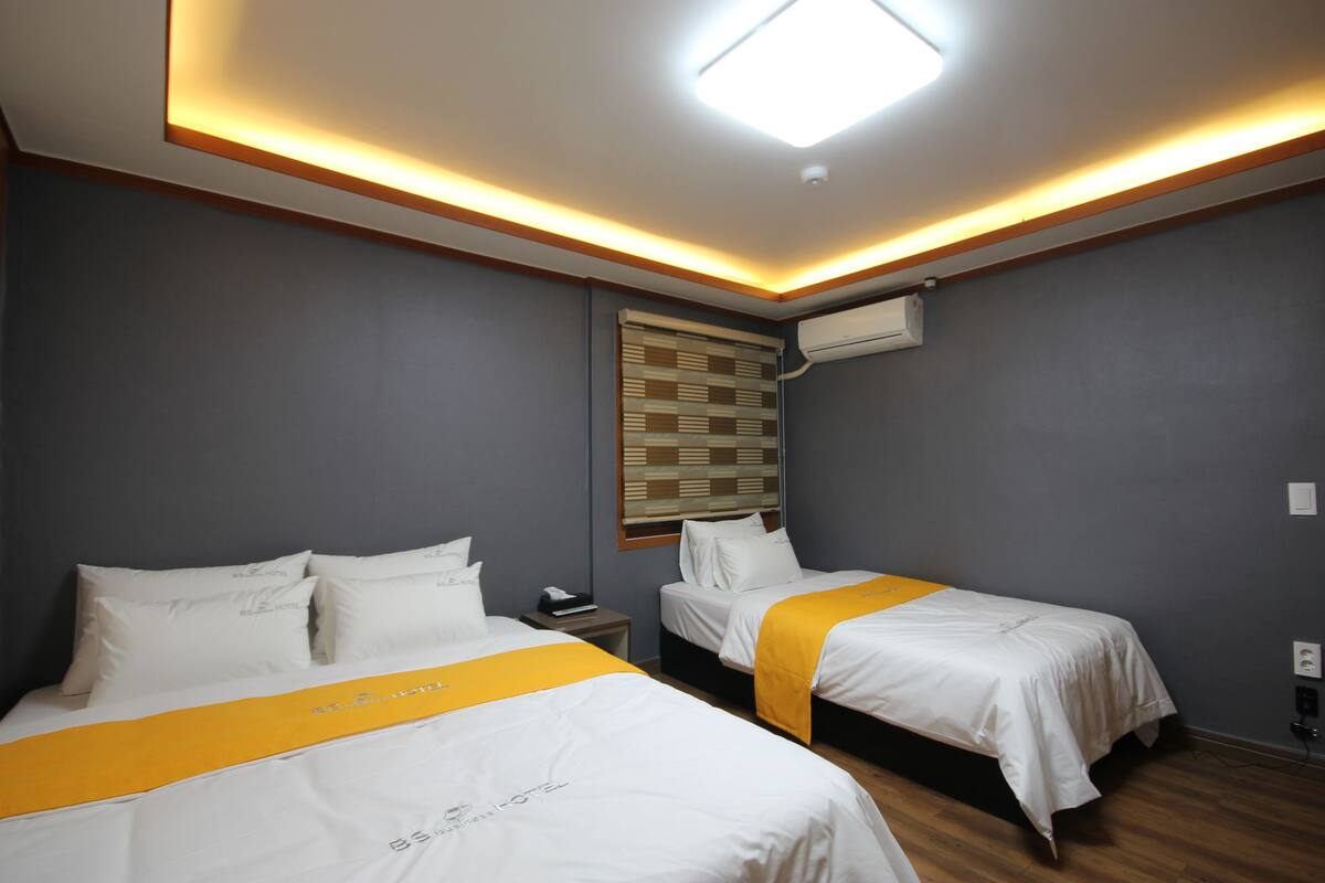Habitación de hotel con dos camas, una lámpara en el techo, aire acondicionado y una ventana con persianas.