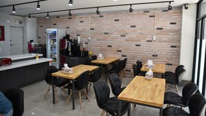 A modern cafe with brick walls, wooden tables, black chairs, and a counter with a refrigerator and coffee machine. - BSB Hotel (Busan)