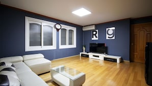 A living room with a white sofa, a glass coffee table, a flat-screen TV, and a wooden floor. - BSB Hotel (Busan)