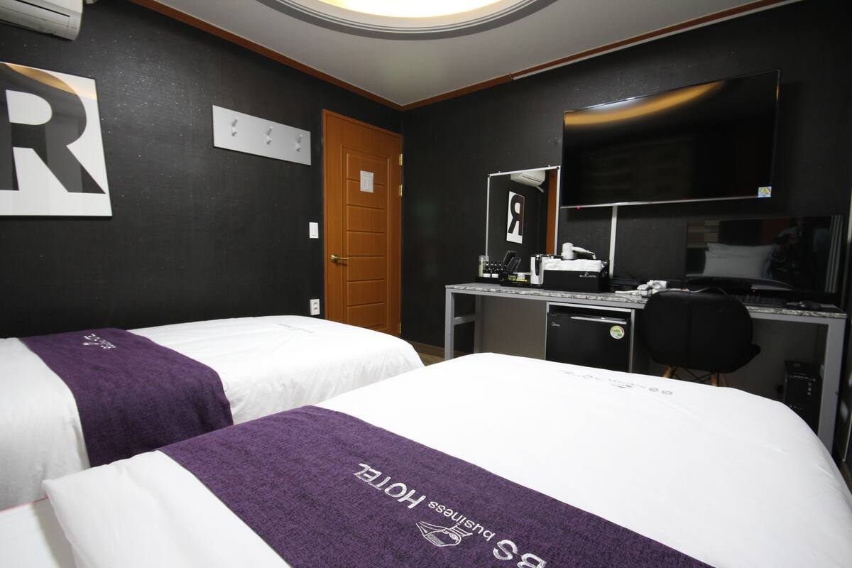 A hotel room with two beds, a desk with a computer, a chair, and a mirror.