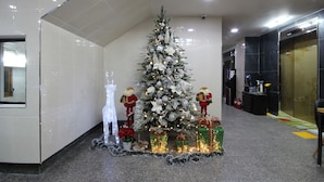 A Christmas tree with ornaments and lights in a hallway with tiled walls and a carpeted floor. - BSB Hotel (Busan)