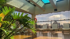 A rooftop terrace with wooden flooring, white lounge chairs, and a large window offering a city view. - Travel Inn Flats Jardins (São Paulo)